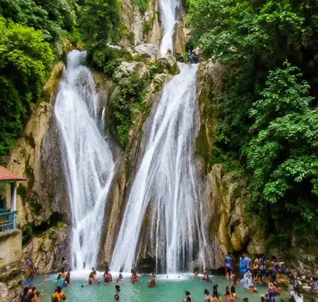 Kempty Falls in Mussoorie surrounded by lush green hills with cascading waterfall and tourists enjoying the scenic beauty